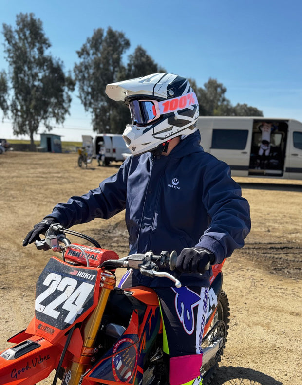Person on a dirt bike wearing protective gear and a Hestiia 7k1 dark blue bomber jacket in an outdoor setting