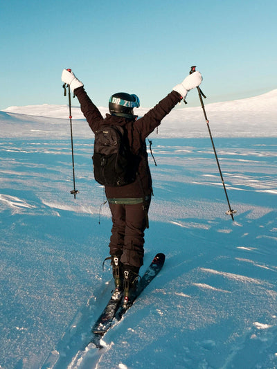 Person skiing in a snowy landscape with arms raised against a clear blue sky