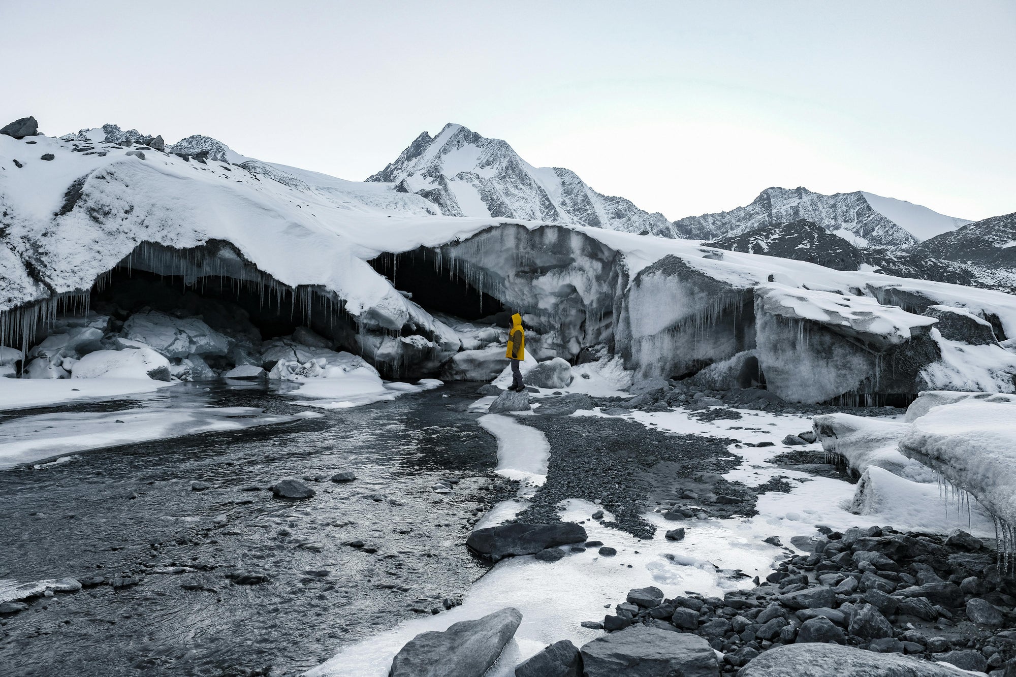 Person in a yellow and black Hestiia 7k3 jacket standing on a frozen landscape with ice formations and mountains.