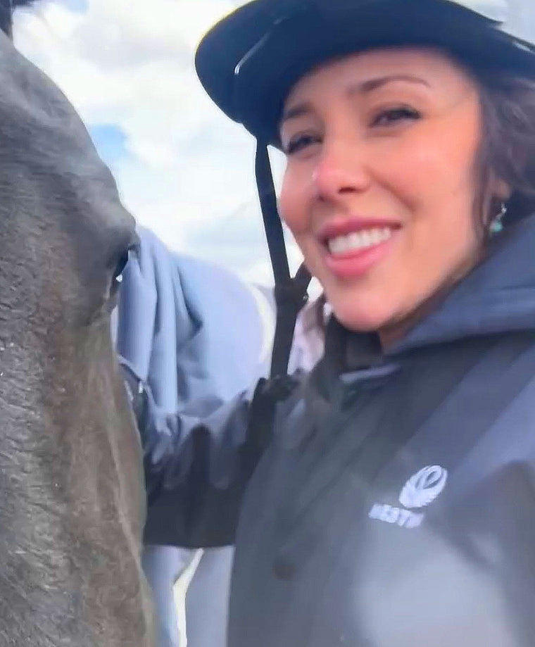 Woman in a jacket and helmet interacting with a horse outdoors